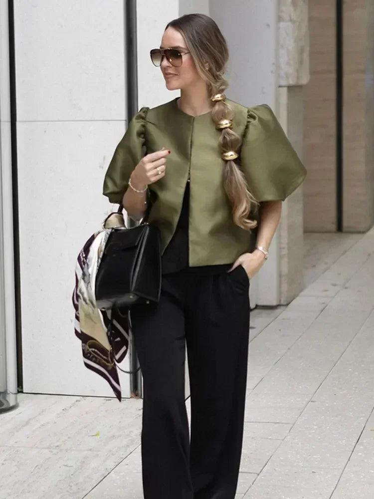 Woman in green top and black pants walking outdoors on a city street.