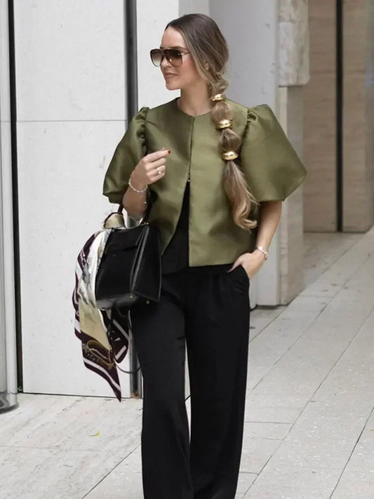 Woman in green top and black pants walking outdoors on a city street.