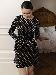 Woman wearing a black polka dot dress standing in a bedroom.