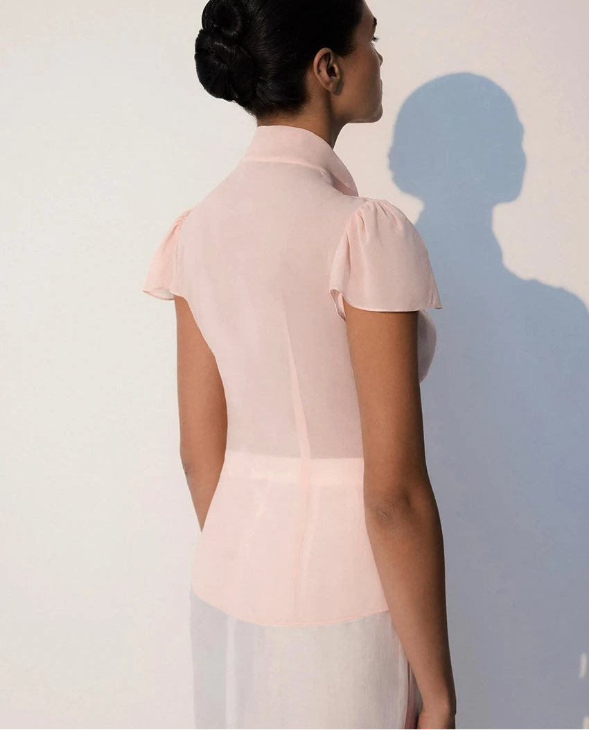 Woman wearing a light pink blouse with short sleeves against a plain background