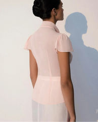 Woman wearing a light pink blouse with short sleeves against a plain background
