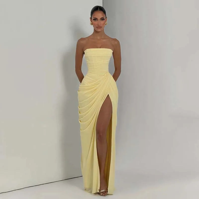 Woman wearing a yellow strapless gown with a high slit on a plain background