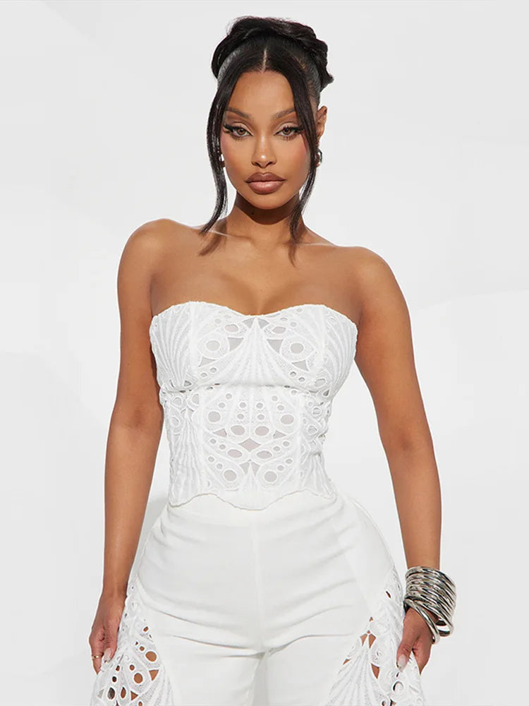 Woman wearing a white strapless outfit with intricate detailing on a plain background