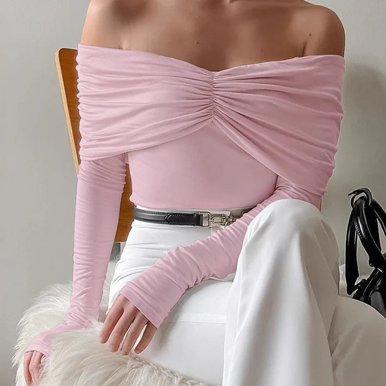 Person wearing a pink off-shoulder top and white pants sitting on a chair.