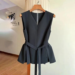 Black sleeveless top with a belt on a wooden hanger against a white wall.