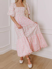 Woman wearing a pink floral dress standing against a white wall.