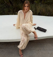 Woman in a beige outfit sitting on a white bench with a black clutch.