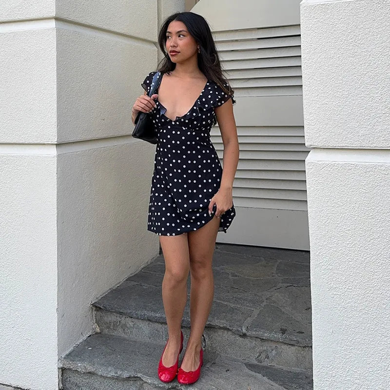 Woman in a black polka dot dress standing on steps with a neutral background