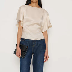 Person wearing a beige blouse and blue jeans holding a black clutch against a white background