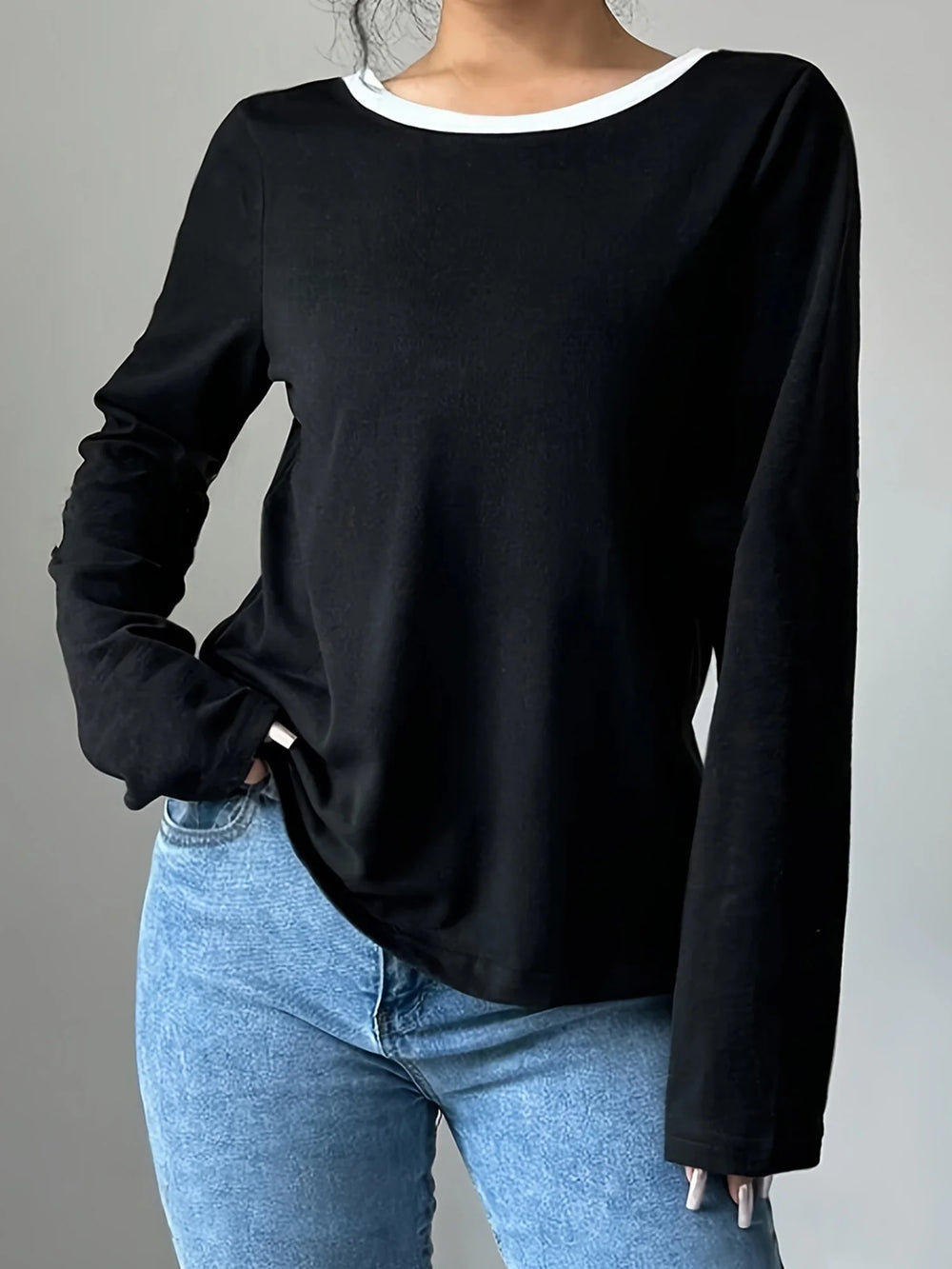 Person wearing a black long-sleeve top and blue jeans on a gray background