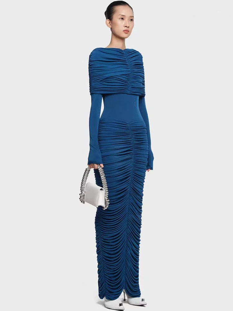 Woman wearing a blue ruched dress holding a white handbag on a light gray background