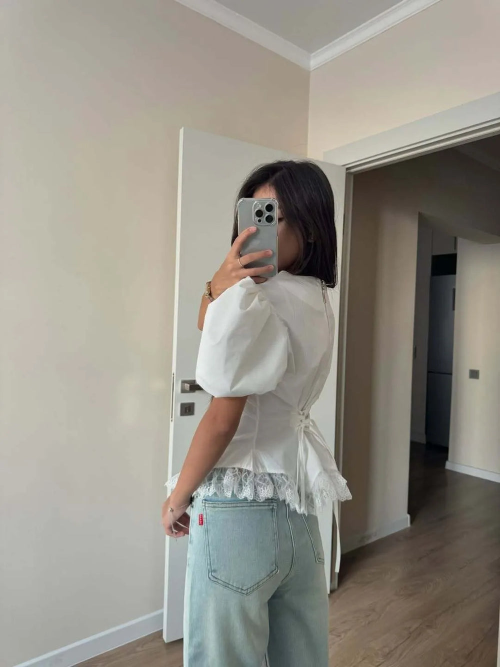 Person wearing a white blouse with puffed sleeves and light blue jeans taking a mirror selfie.