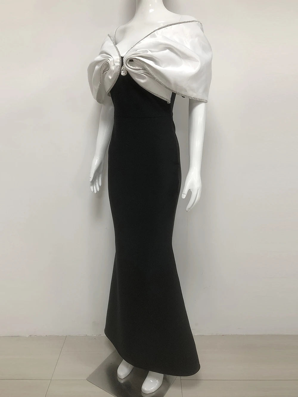 Mannequin wearing a black evening gown with a silver bow detail on a white background