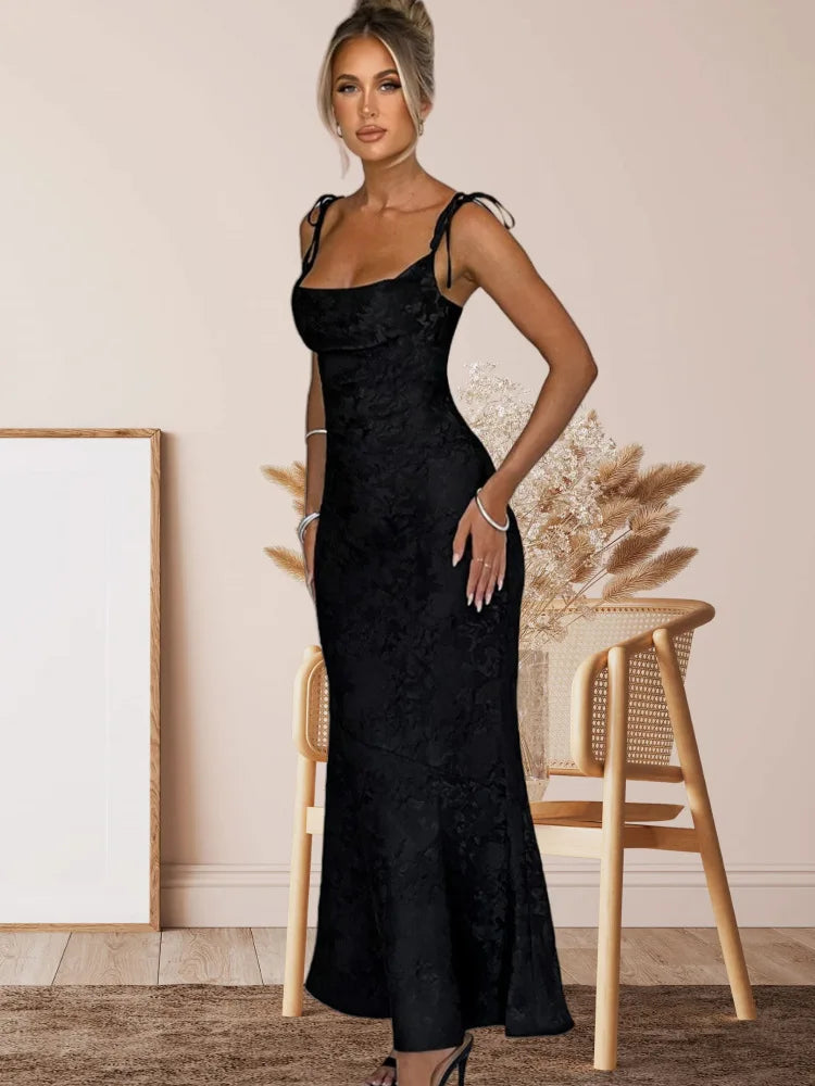 Woman wearing a black dress standing in a room with a chair and decorative elements.