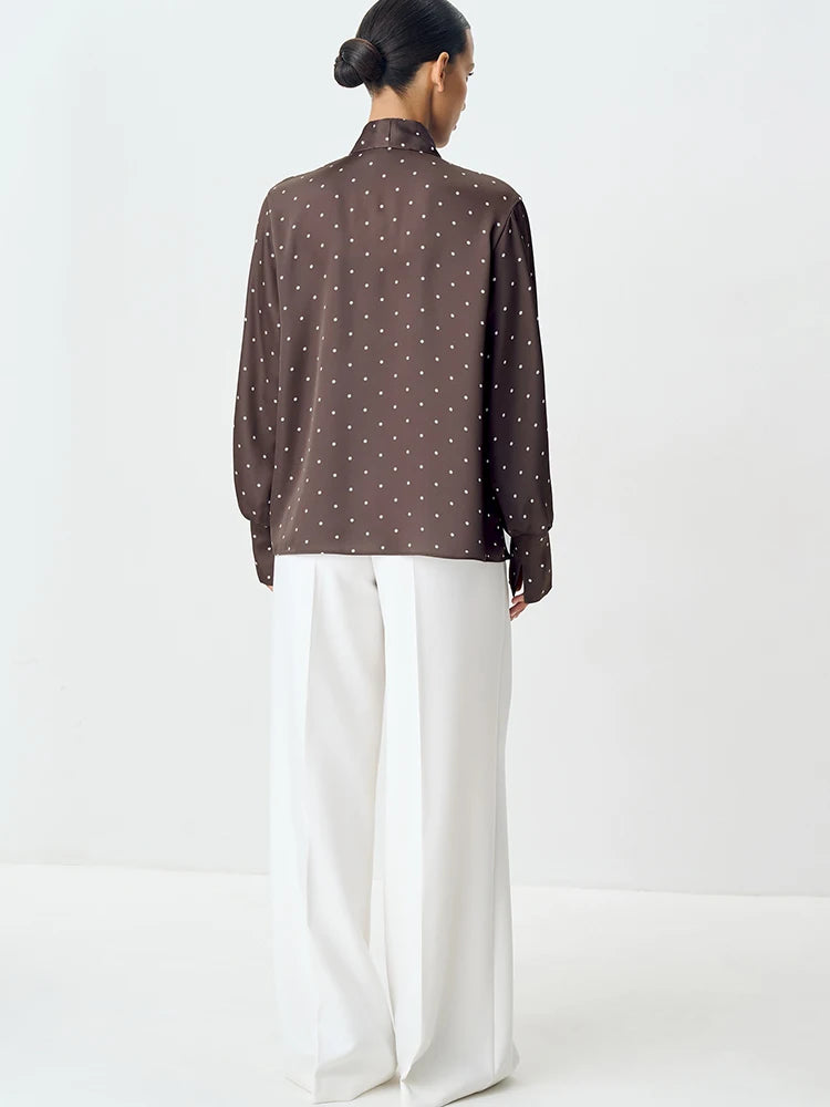 Person wearing a brown polka dot blouse and white pants on a white background