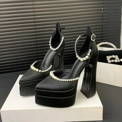 Black high-heeled shoes with pearl embellishments on a white platform against a black background.