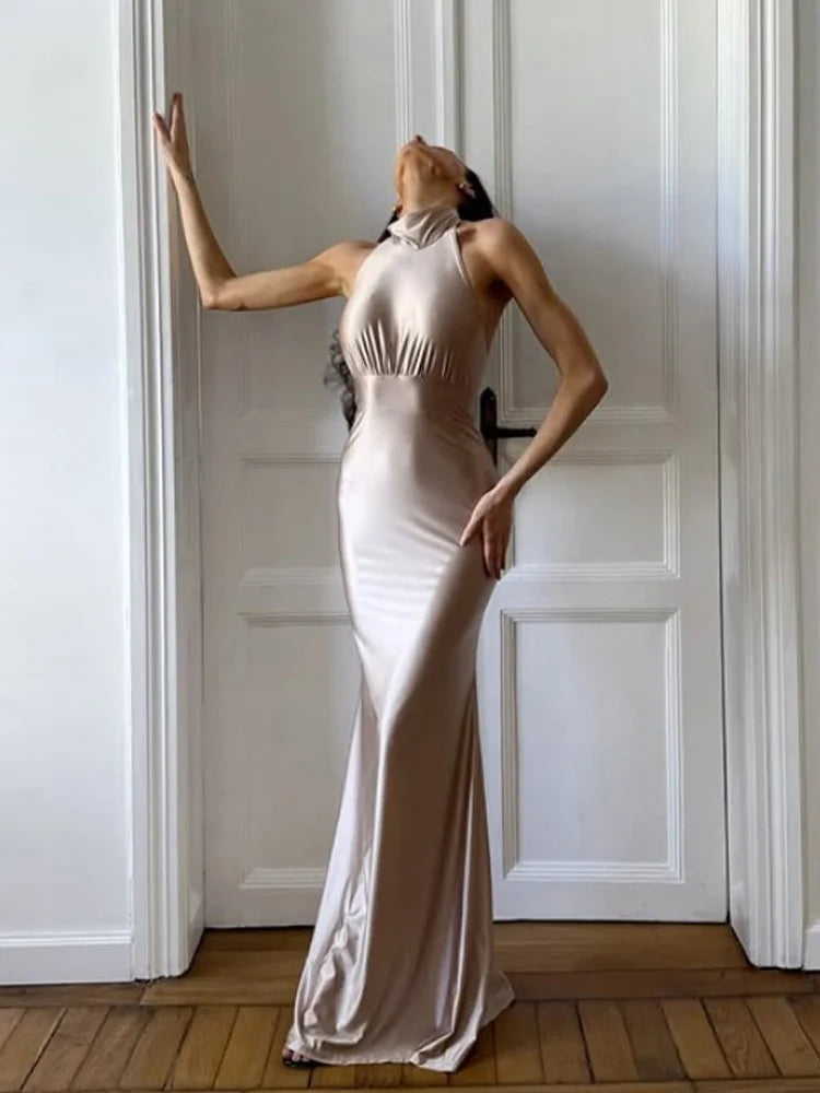 Woman in a white evening gown standing against a white paneled wall.