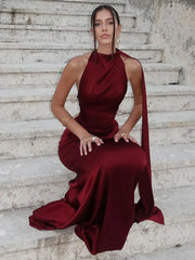 Woman in a burgundy halter neck gown sitting on stone steps.