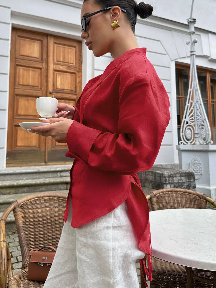Woman in a red jacket holding a cup outdoors with a building in the background