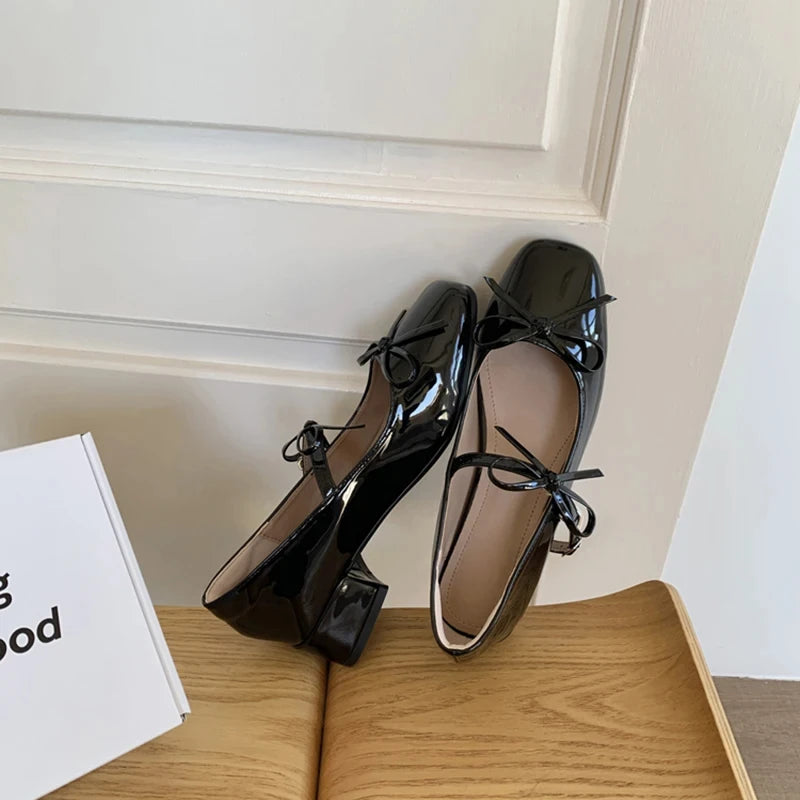 Black patent leather shoes with bow details on a wooden surface.