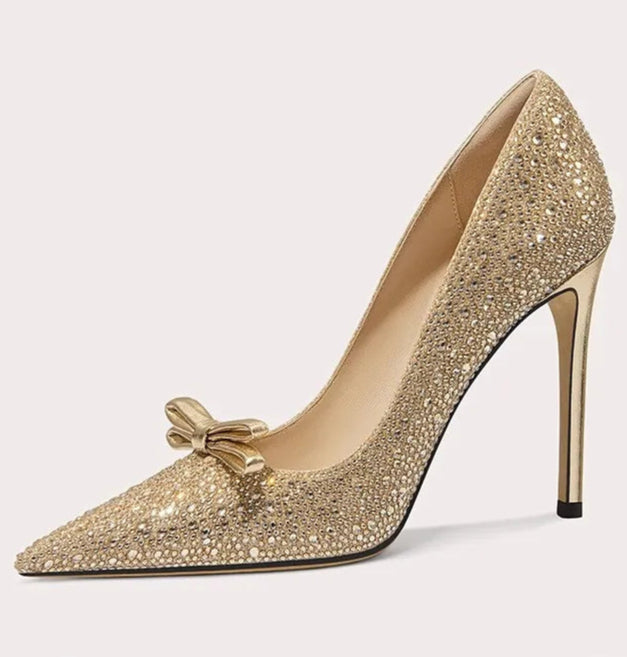 Gold high-heeled shoe with decorative bow on a light gray background