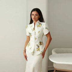Woman wearing a white floral blouse and skirt in a minimalistic room.