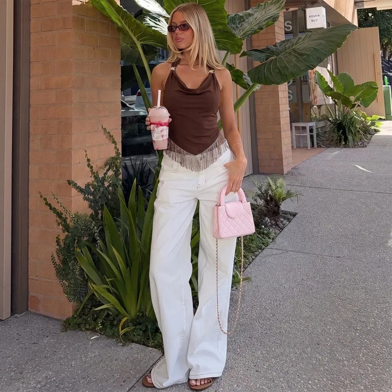 Woman in white pants holding a pink drink and pink handbag wearing a brown halter neck top with fringe