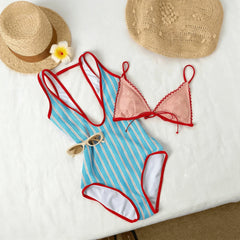 Blue and white striped one-piece swimsuit with red trim, pink lace bikini top, straw hat, sunglasses, and flower