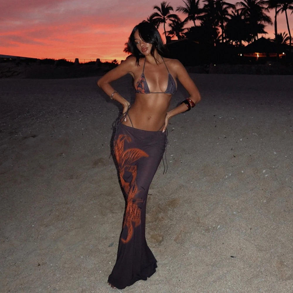 Woman in a dark dress with orange patterns on a beach at sunset