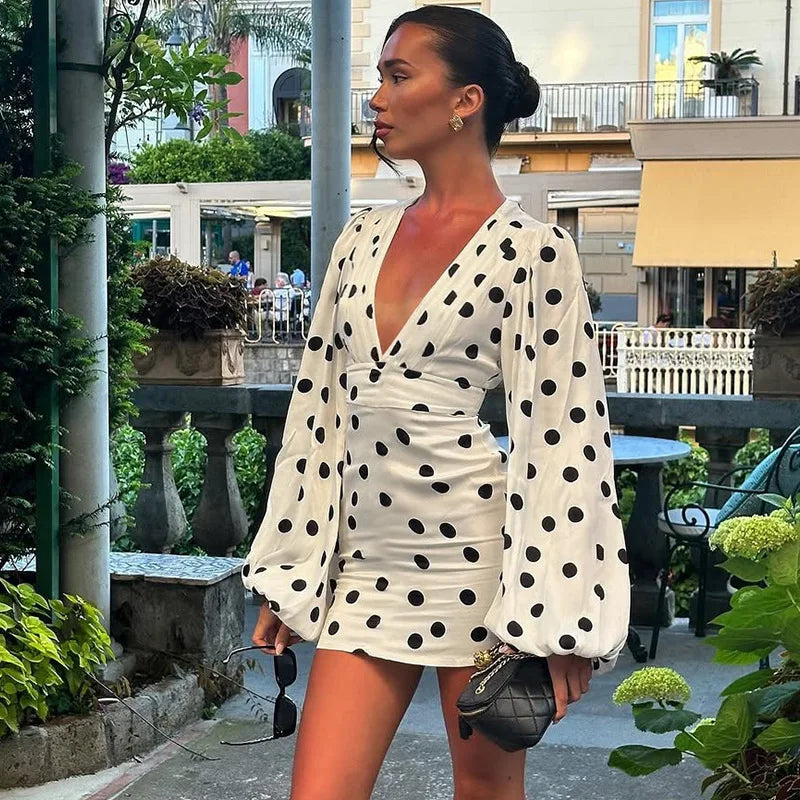 Woman in a polka dot dress standing outdoors with buildings and greenery in the background