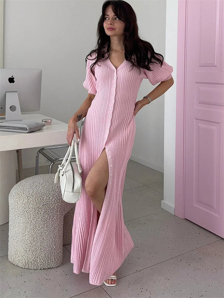 Woman in a pink dress standing in a room with a desk and computer.