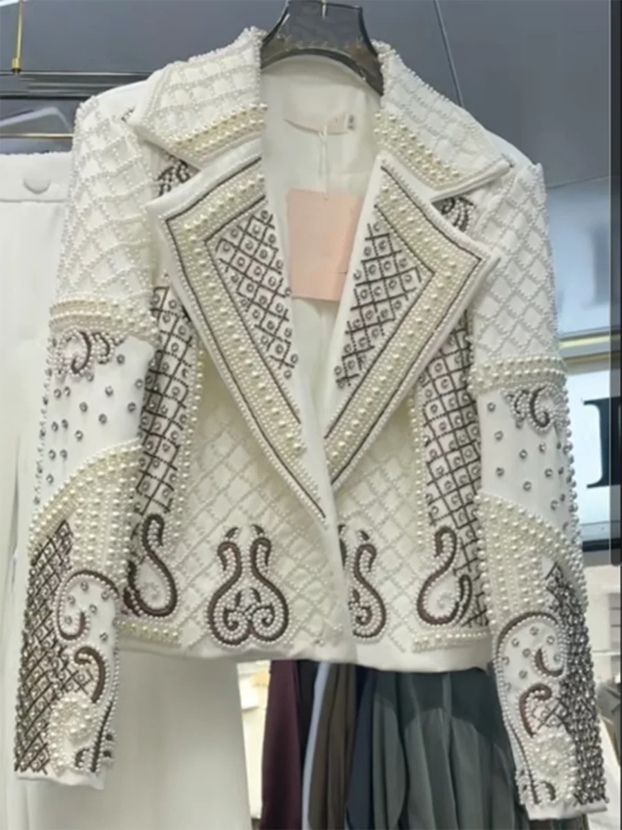 Elegant white jacket with intricate black patterns on a hanger against a blurred background