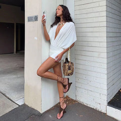Woman in a white outfit leaning against a white wall.