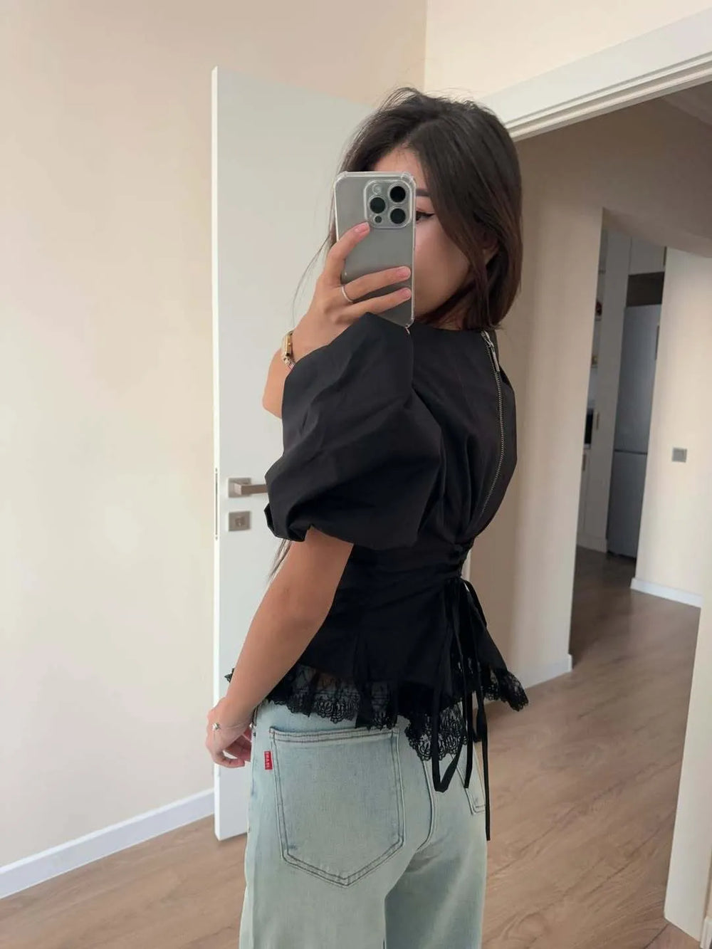 Person wearing a black top with lace details and light blue jeans in a room.