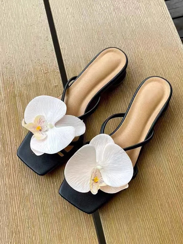 Black sandals with white orchids on a wooden surface