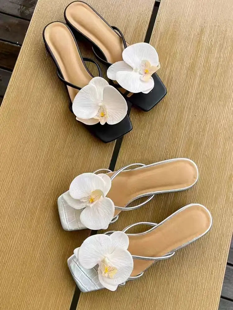 Black and silver sandals with white orchids on a wooden surface