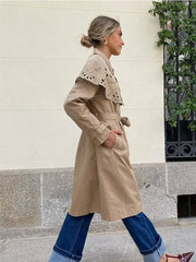 A stylish woman wearing a double-breasted trench coat with a shawl collar and belt, showcasing its elegant design.