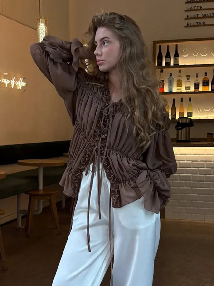Woman in a brown blouse and white pants standing in a restaurant setting.