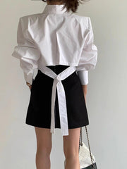 Person wearing a white blouse with ruffled sleeves and a black skirt against a plain background