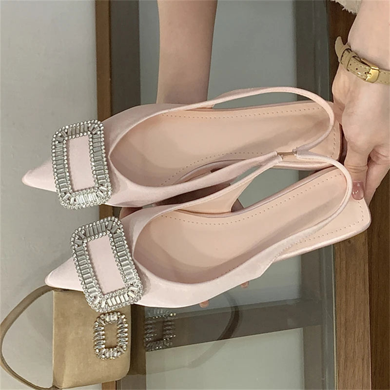 Beige flat shoes with embellishments held by a person against a neutral background