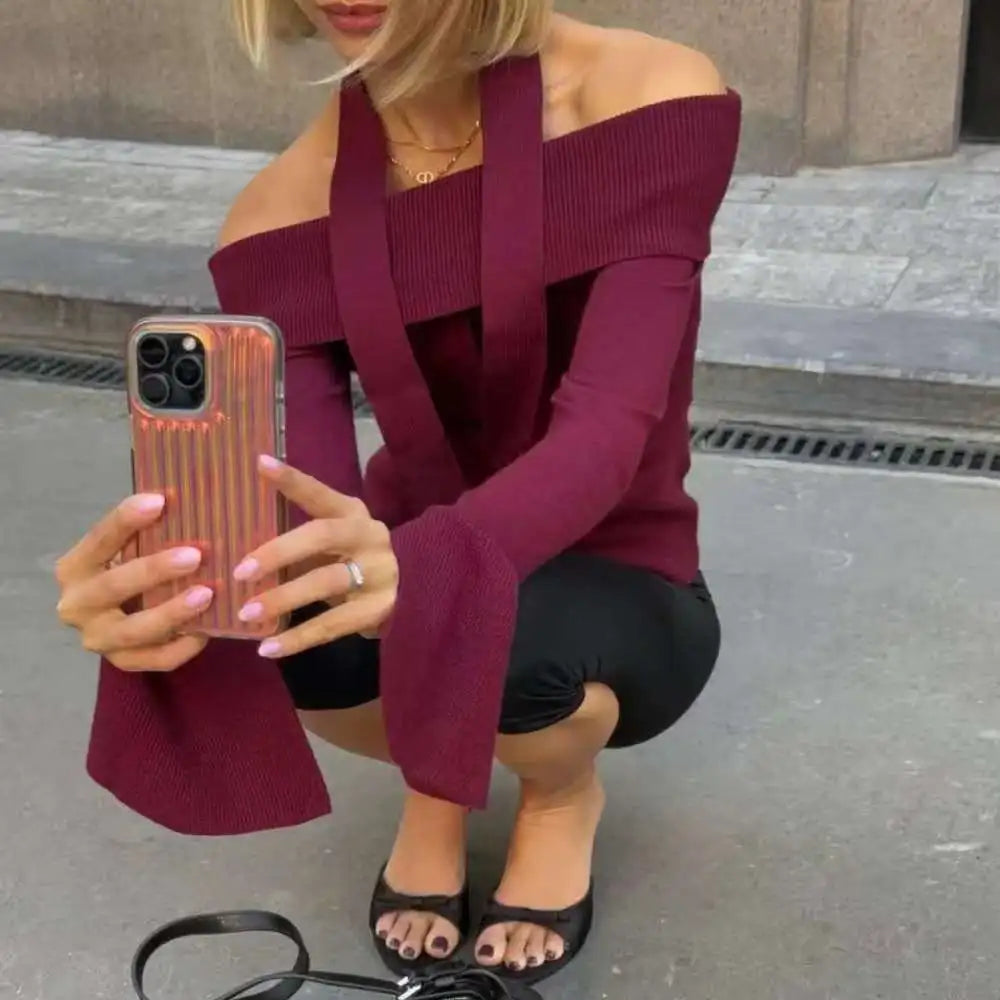Woman in a burgundy off-shoulder top taking a selfie on a city street.