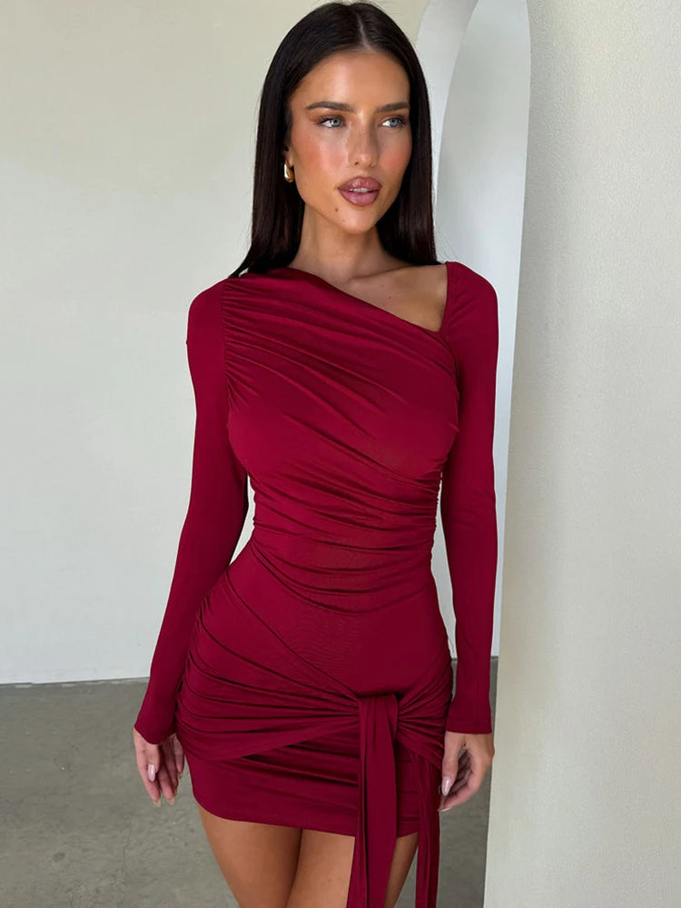 Woman wearing a burgundy dress with long sleeves against a white wall.