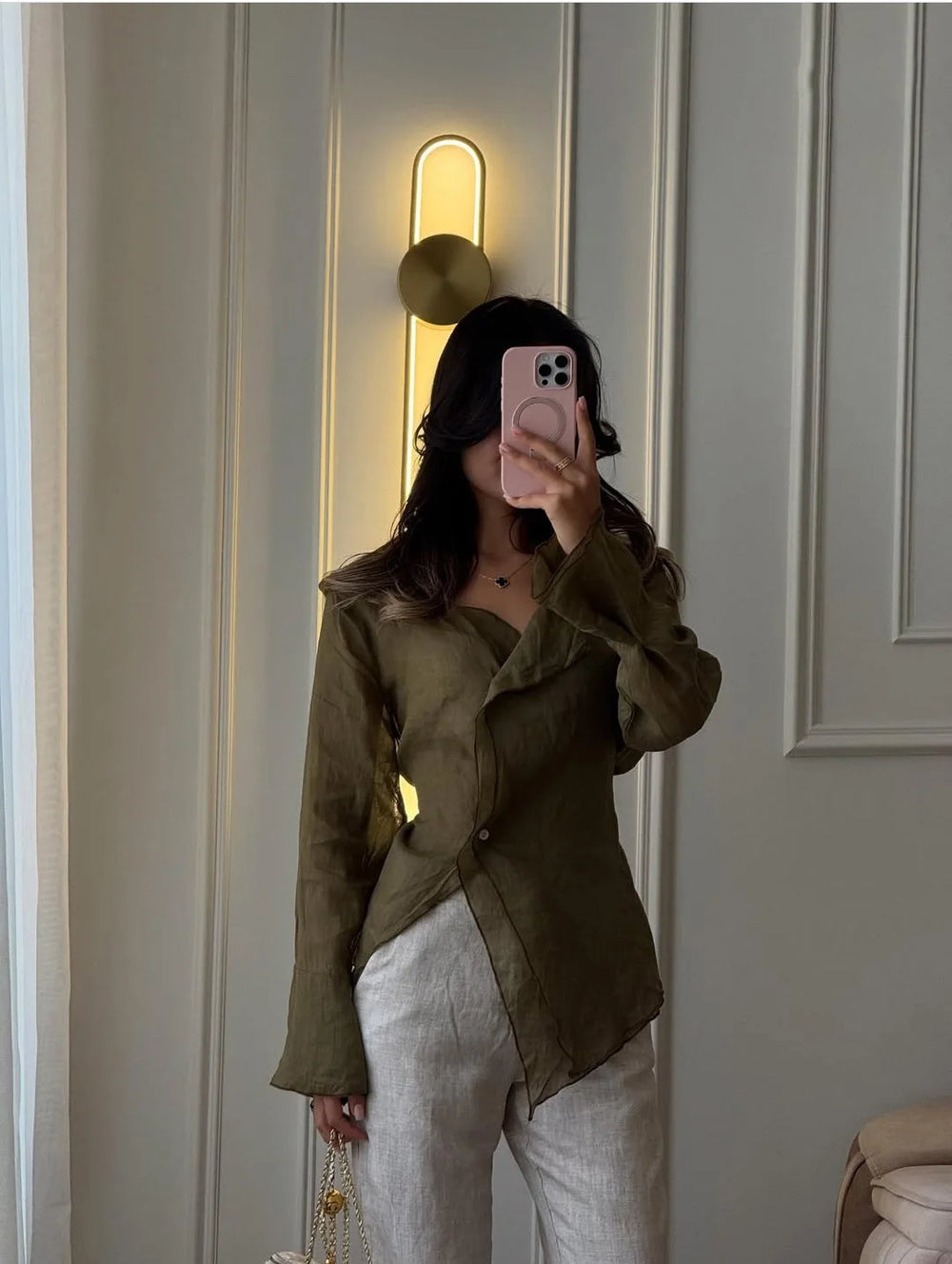 Person wearing a green jacket and white pants taking a mirror selfie.