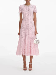 Woman wearing a pink lace dress holding a matching handbag on a white background