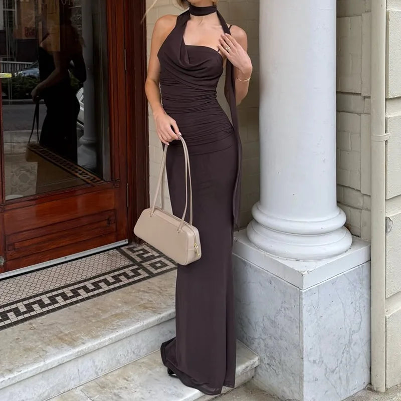 Woman in a brown dress holding a beige handbag, standing in front of a building entrance.