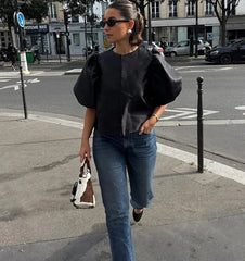 Woman in black top and blue jeans walking on a city street.