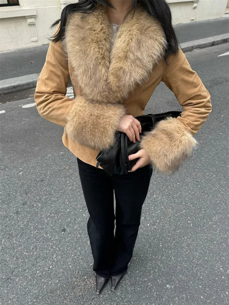 Person wearing a tan coat with fur collar and cuffs on a street.