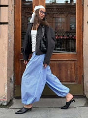 Person wearing a black jacket, white top, blue striped pants, and black shoes in front of a wooden door.