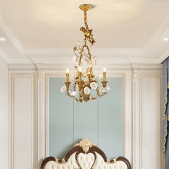 Gold chandelier with floral design in a room with white walls and a mirror.