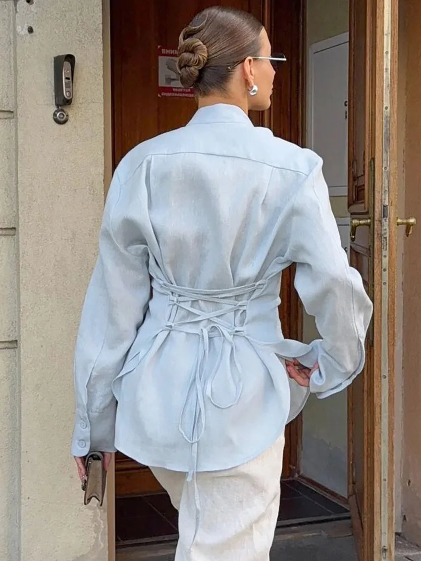 Person wearing a light blue jacket with a tie waist, standing in front of a door.
